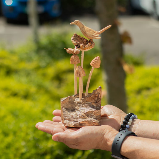 Handmade Parasite Wood Art Carving Bird & Bee on Mushrooms held in hands with a blurred natural background