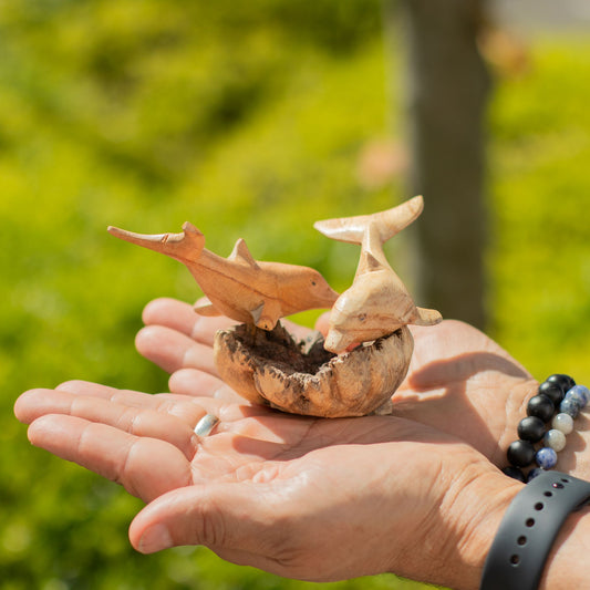 Handmade Parasite Wood Art Carving Dolphins in Play against a blurred green outdoor background