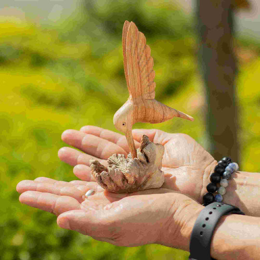 Handmade Parasite Wood Art Carving Nectar Drinking Hummingbird on a person's hand with a blurred green outdoor background