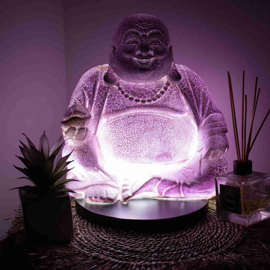 Laughing Buddha Lamp Lavender Crackle with the light turned on with a dark background.