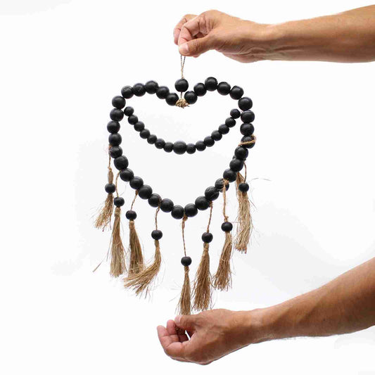 Black beaded wall hanging with tassels held by a person against a white background