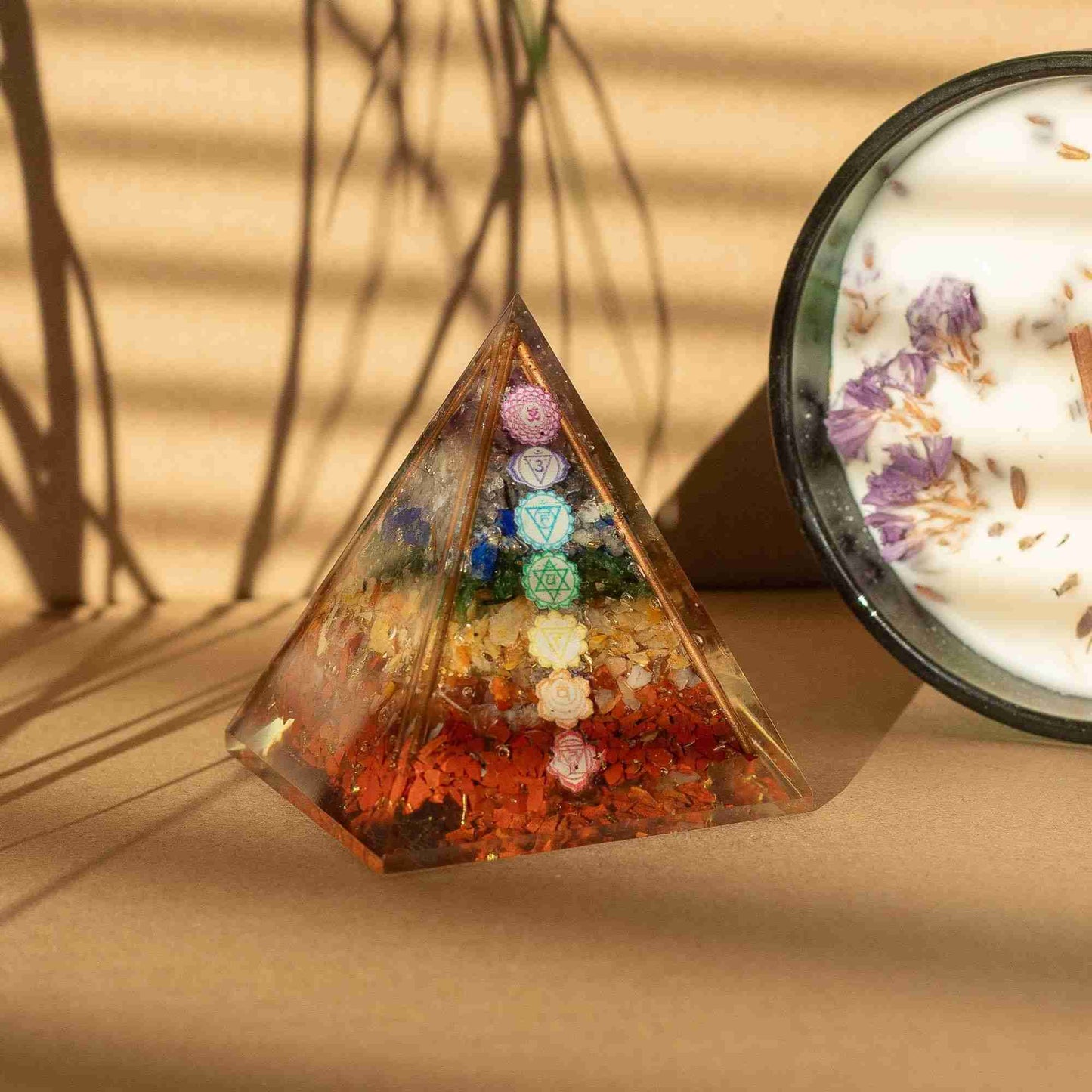 Pyramid-shaped crystal with colorful stones and a candle with flowers on a beige surface
