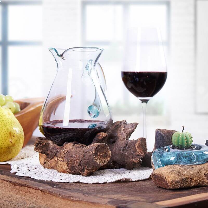 Molten Glass on Wood- Water Jug placed on a wooden table, with fruit, wine, and decorative items surrounding it.
