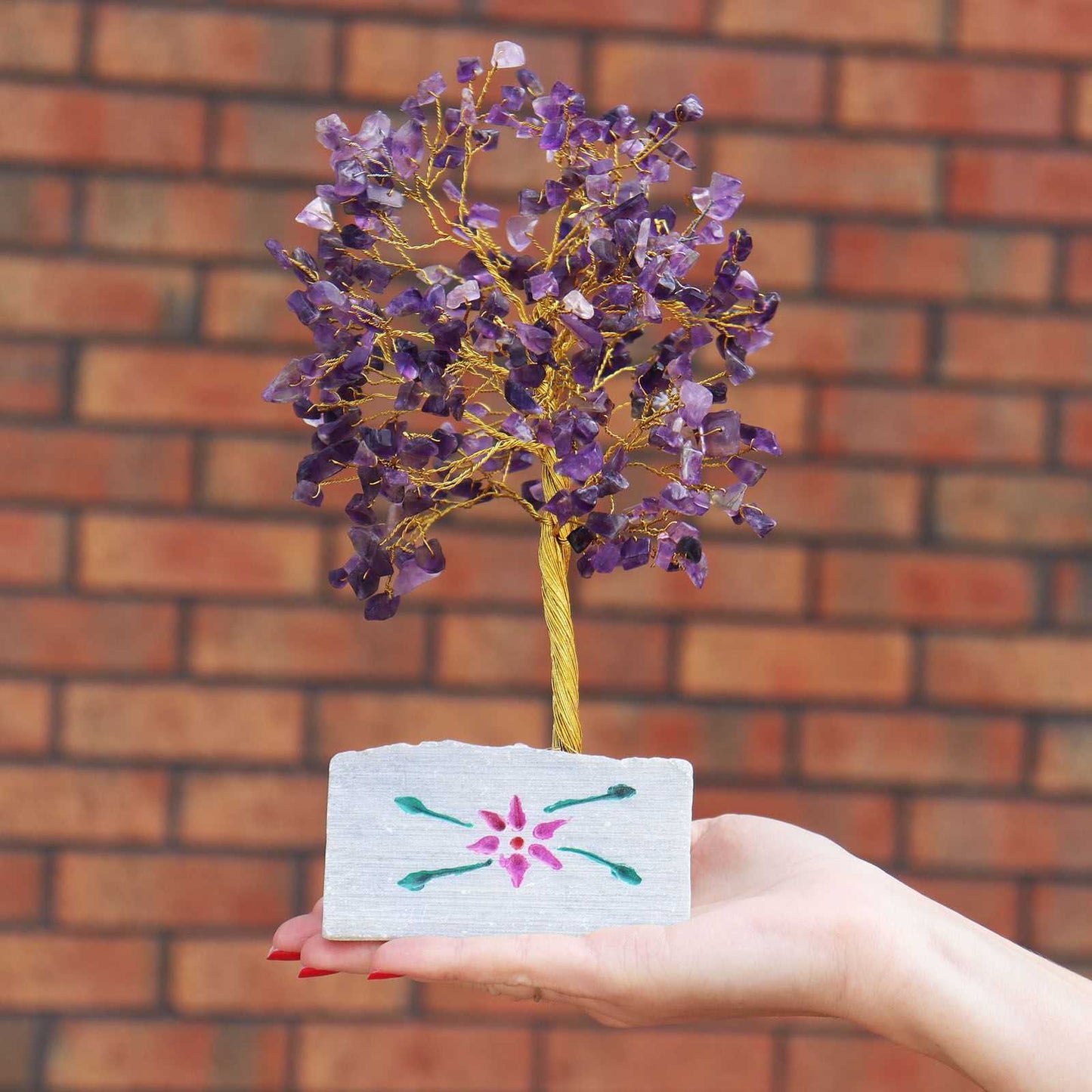 Hand holding an Indian Gemstone Tree - Amethyst (320 Stones) against a brick wall.