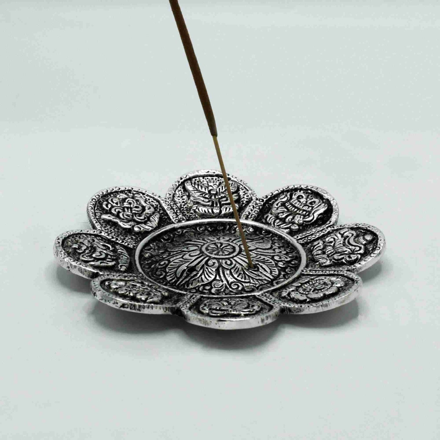 Decorative silver incense holder with a single incense stick on a light gray background