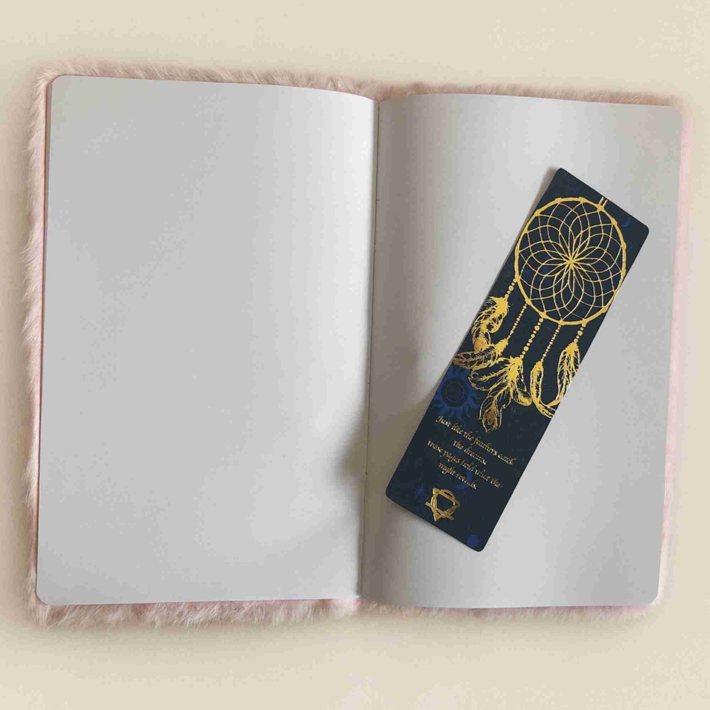 Open notebook with a decorative bookmark featuring a dreamcatcher design on a light pink surface.
