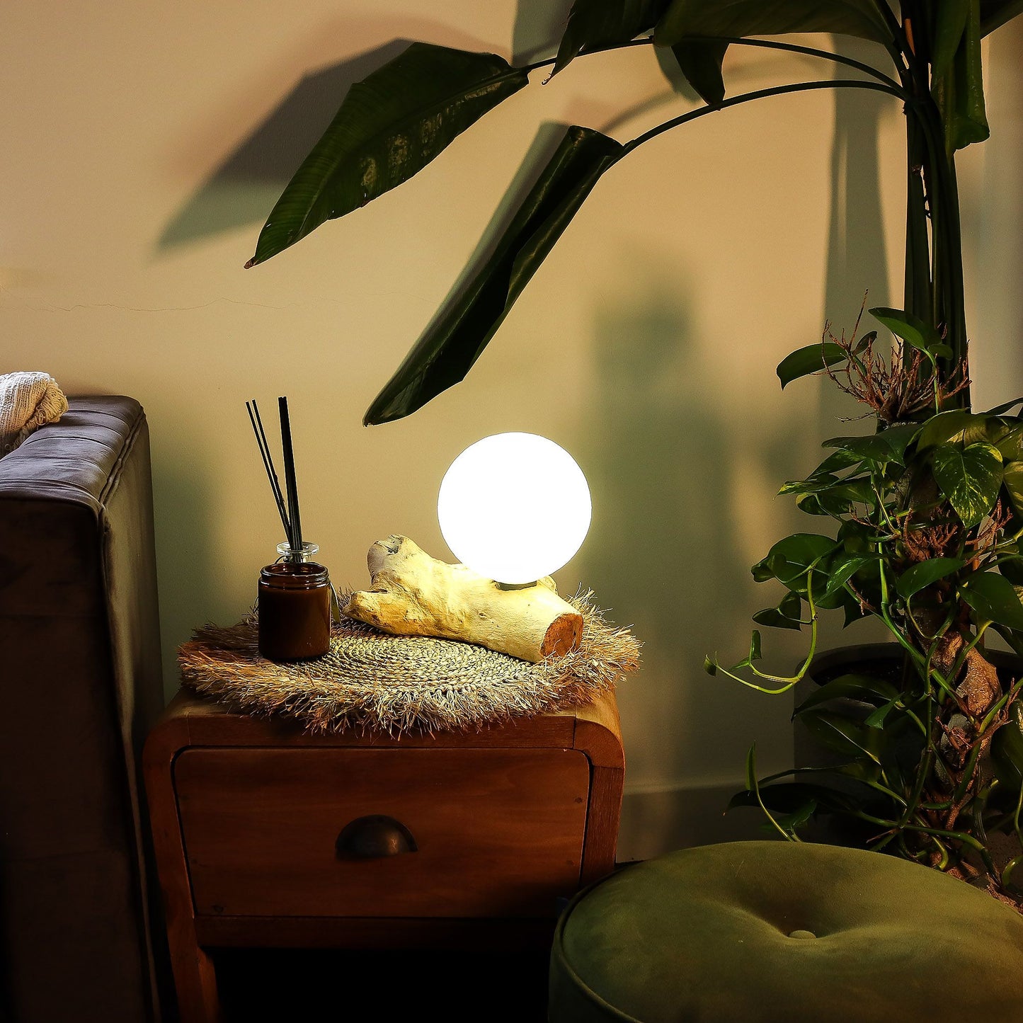 Glowing spherical lamp on a wooden side table with plants and a couch in the background