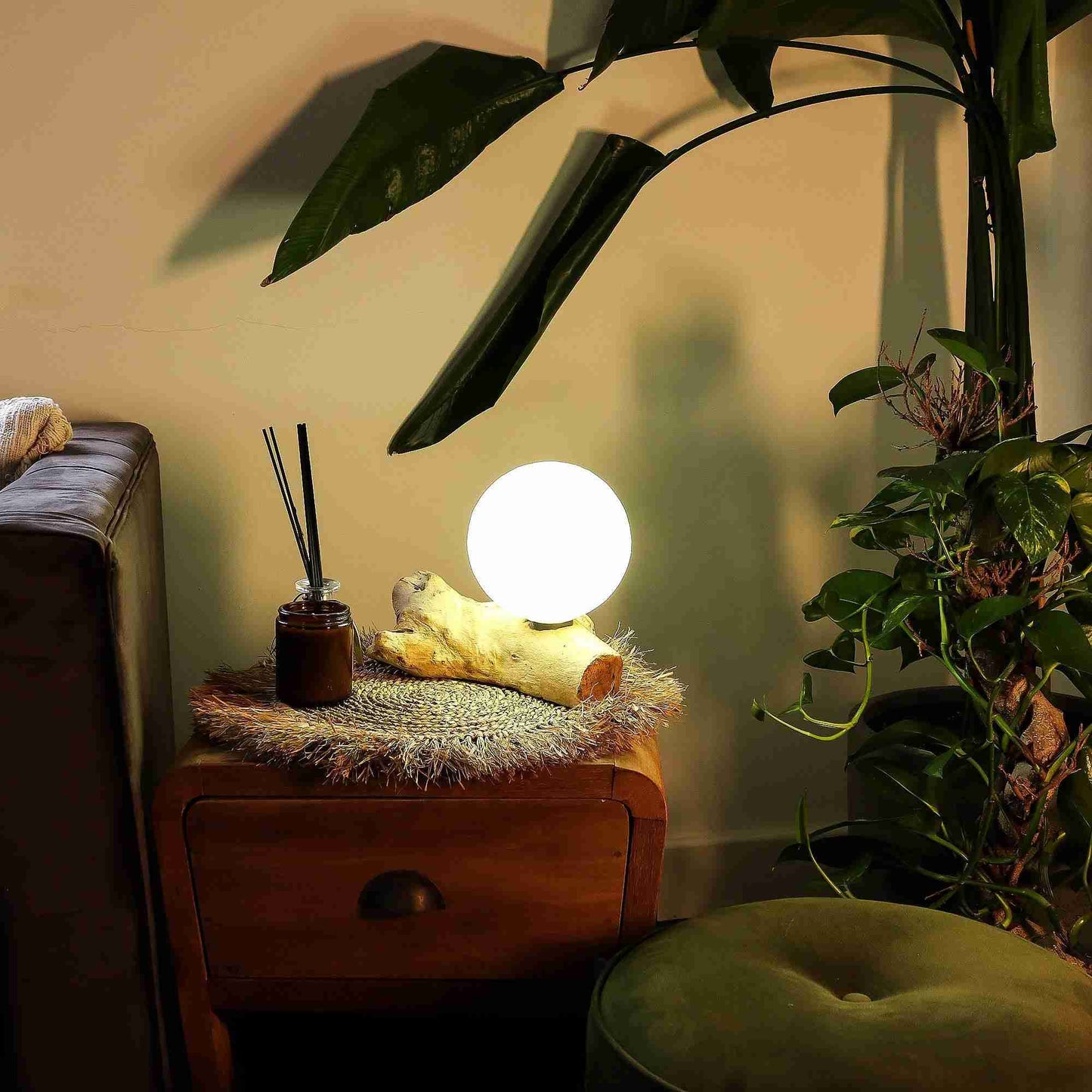 Glowing spherical lamp on a wooden side table with plants and a couch in the background