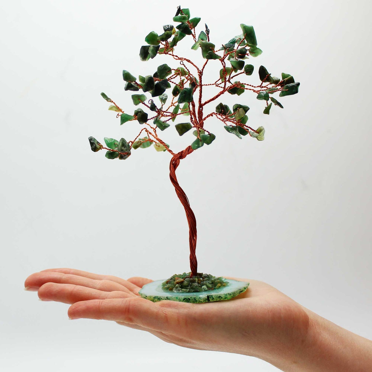 Small tree made of green stones and red branches held in a hand against a white background