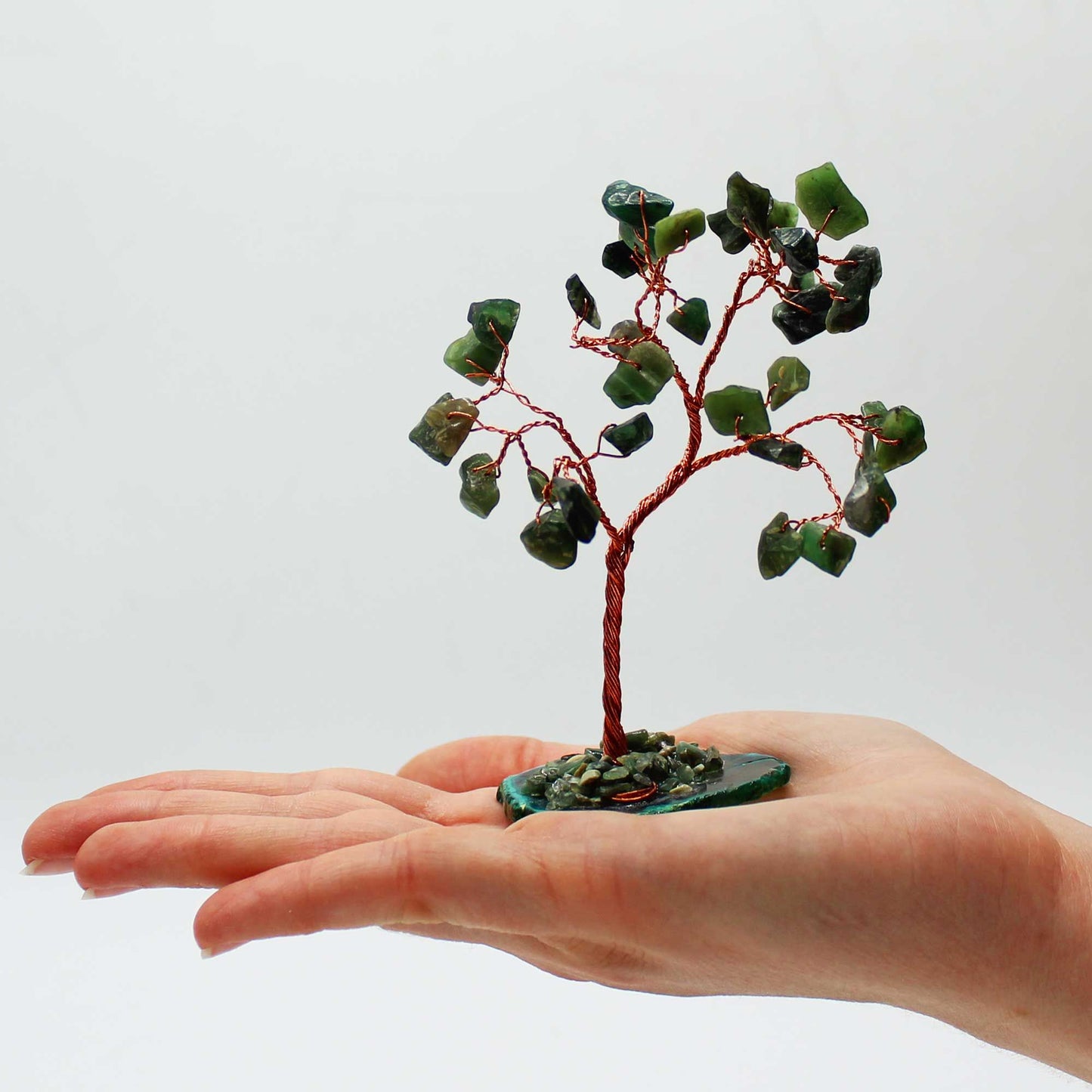Small decorative tree with green stones held in a hand against a light background