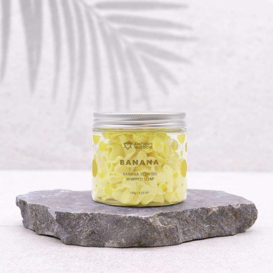 Jar of banana-scented whipped soap on a stone platform with a white background