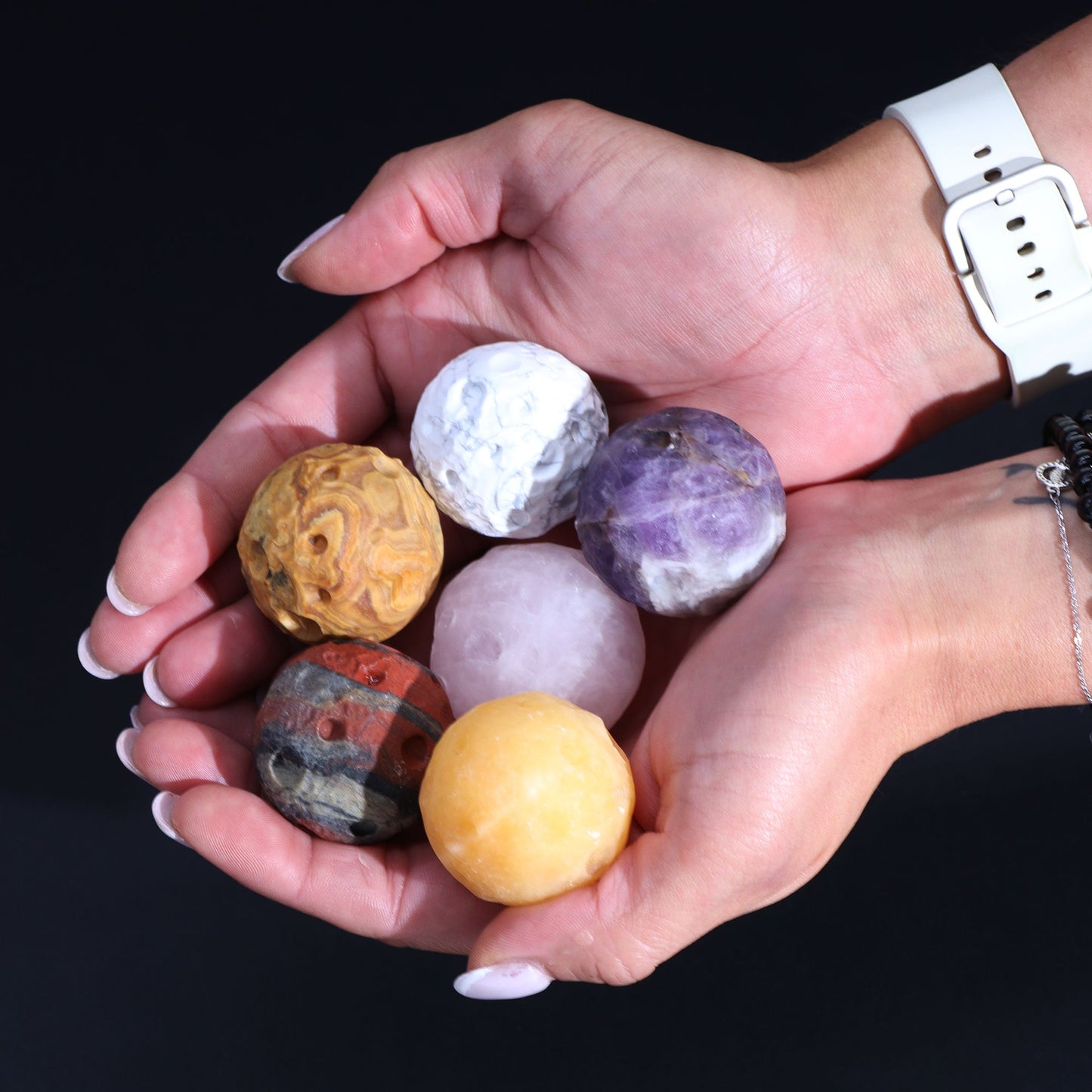 Hands holding a collection of gemstone planets against a black background