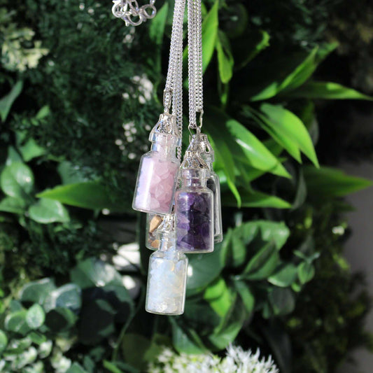 Necklace with three small glass bottles containing different colored stones against a green leafy background