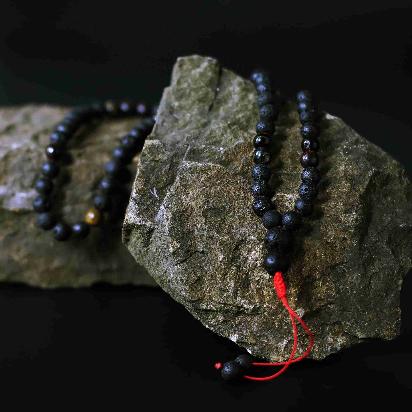 Black beaded necklace with a red string on a dark rock background