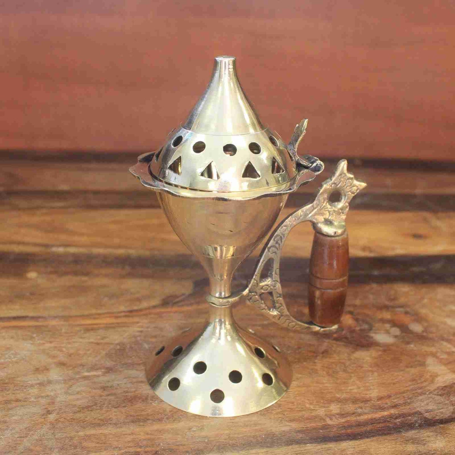 Brass incense burner with wooden handle on a wooden surface