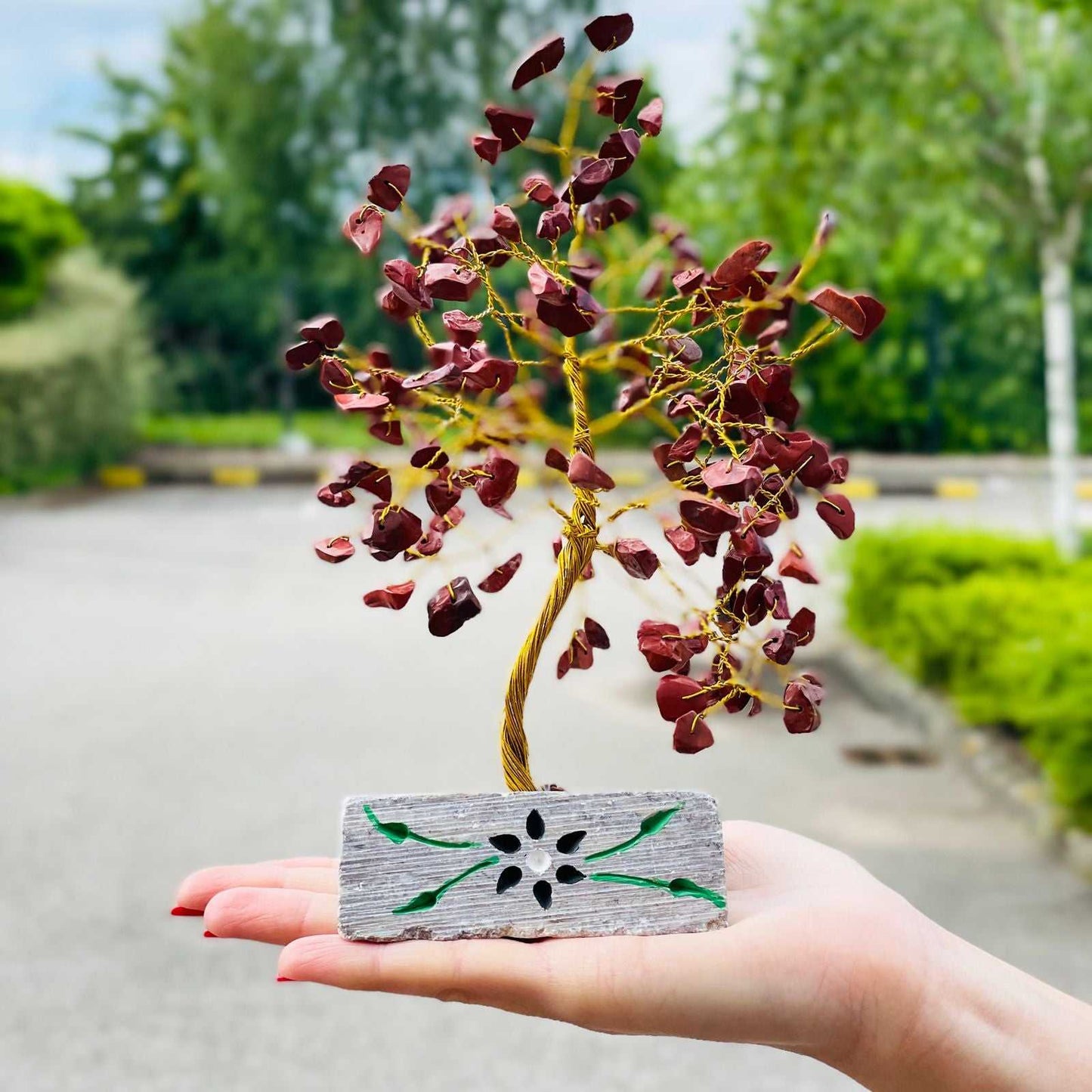 Hand holding a Indian Gemstone Tree - Red Jasper (160 Stones) against a blurred outdoor background.