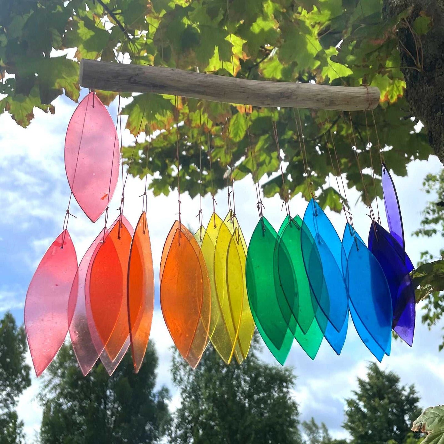 Colorful wind chime hanging from a tree with a clear sky background