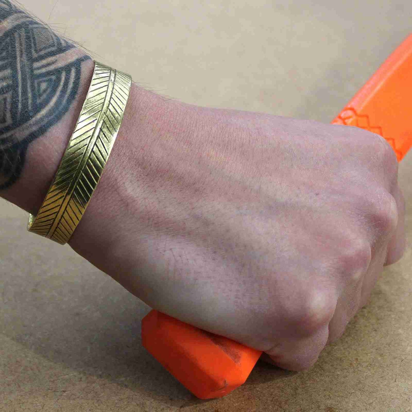 Hand holding an orange object with a Brass Tibetan Bracelet - Wide Tribal Leaf on a beige background