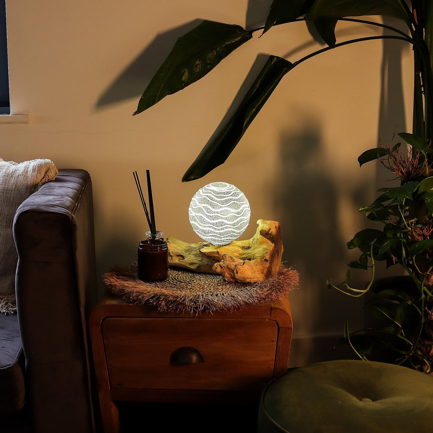 Decorative lamp on a wooden side table with plants and a couch in the background