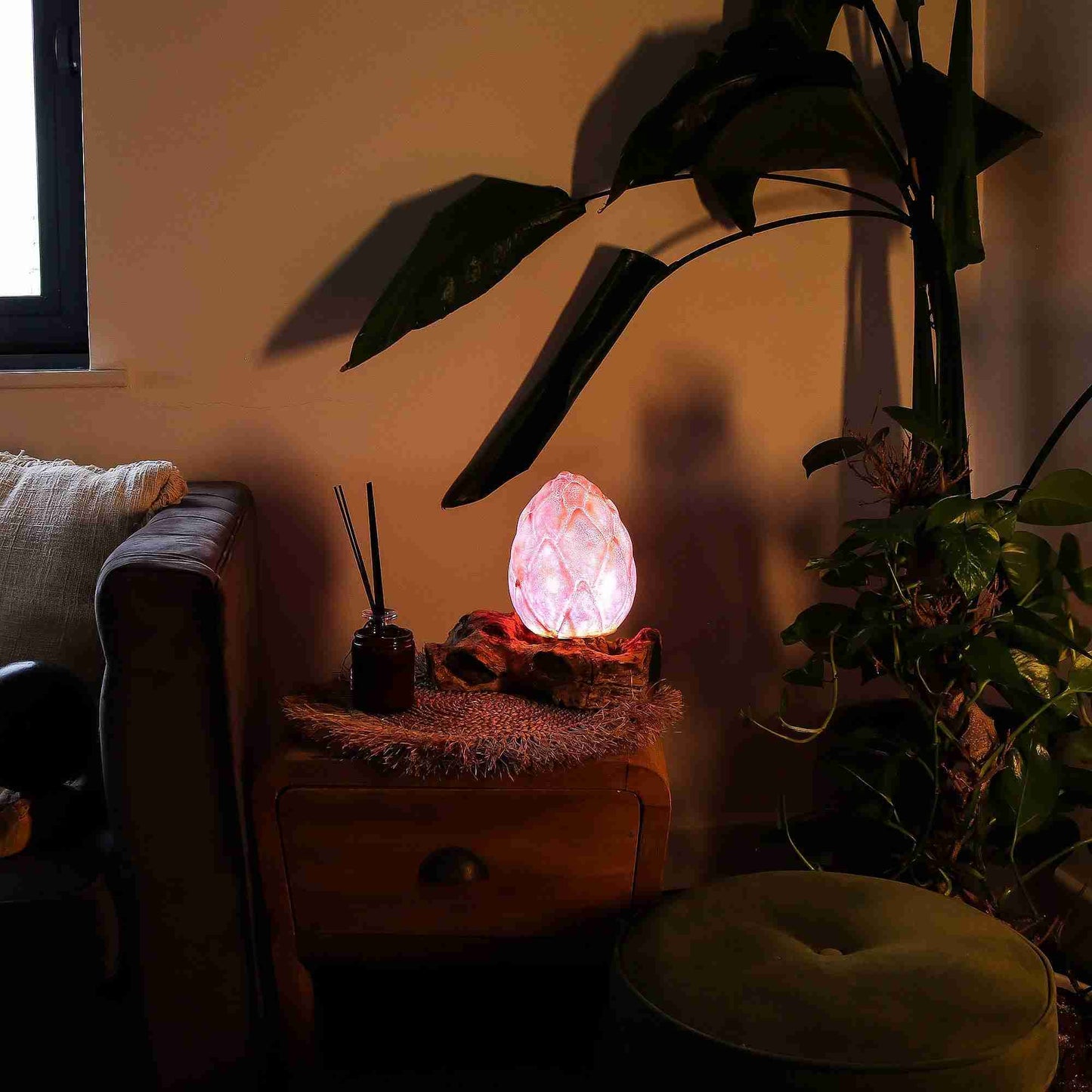 Pink crystal lamp on a side table with a plant and window in a dimly lit room
