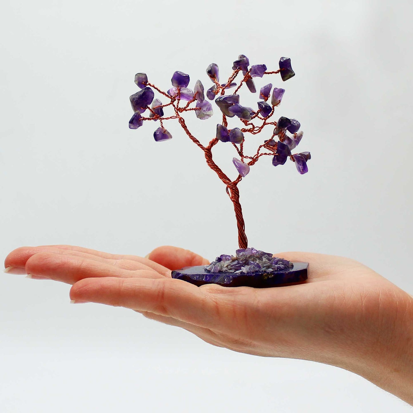 Hand holding a small tree sculpture made of purple stones on a white background