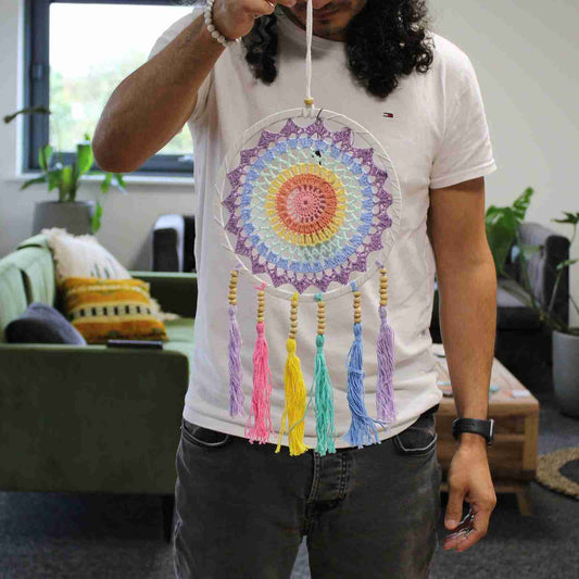 A person wearing a white T-shirt holding a rainbow dreamcatcher.