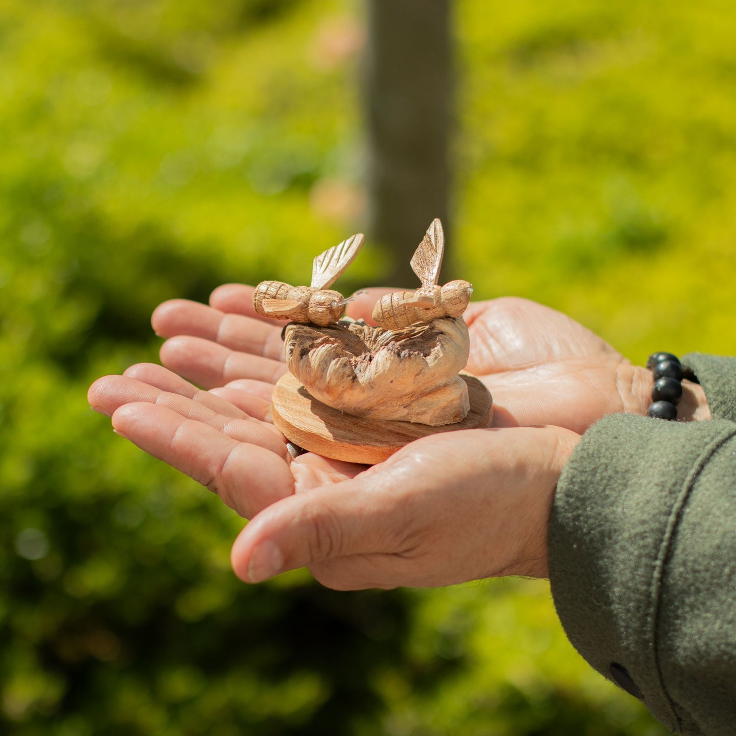 Person holding a Handmade Parasite Wood Art Carving - Bees in The Works against a blurred green outdoor background