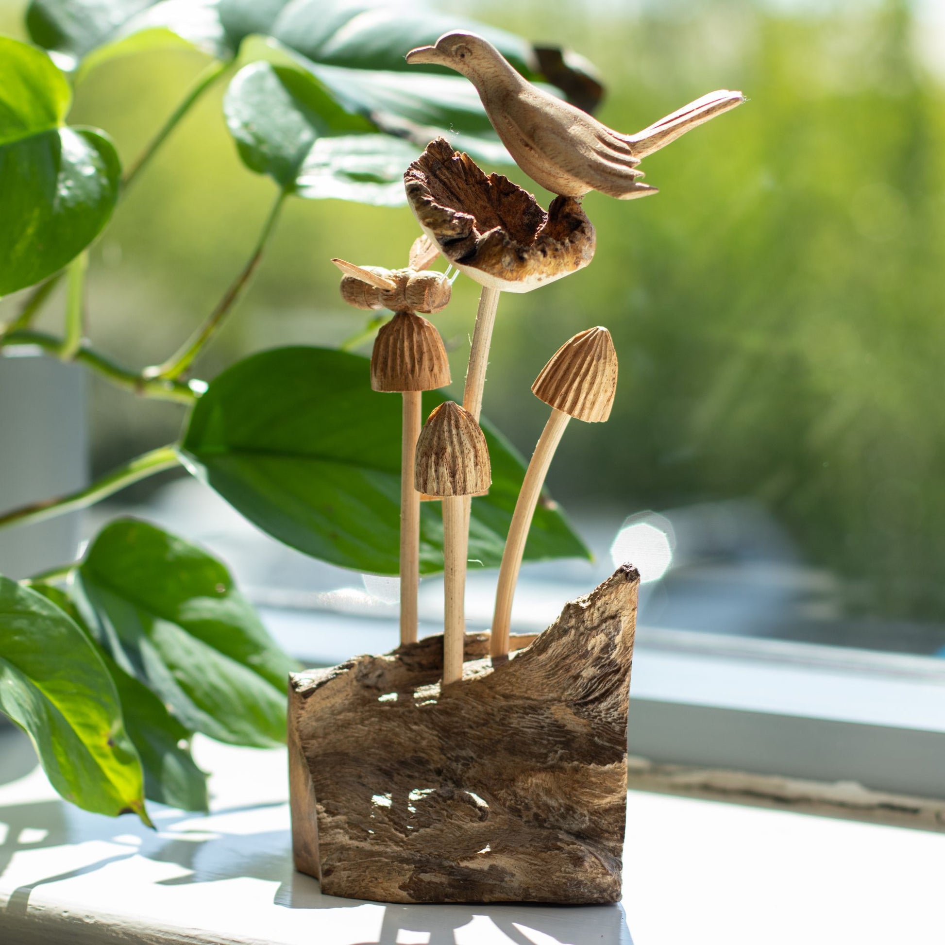 Handmade Parasite Wood Art Carving Bird & Bee on Mushrooms with green foliage and a window in the background