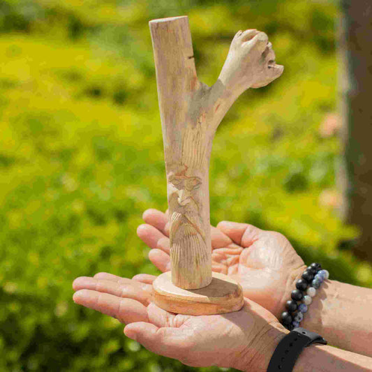 Handmade Parasite Wood Art Carving Greenman, held by hands against a green outdoor background.