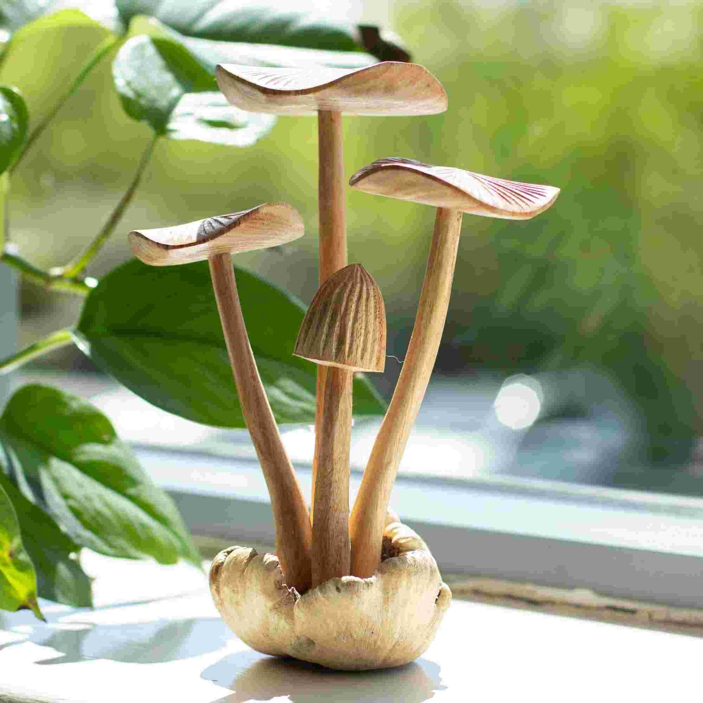 Handmade Parasite Wood Art Carving Set of 4 Large Mushrooms on a light surface with green leaves in the background