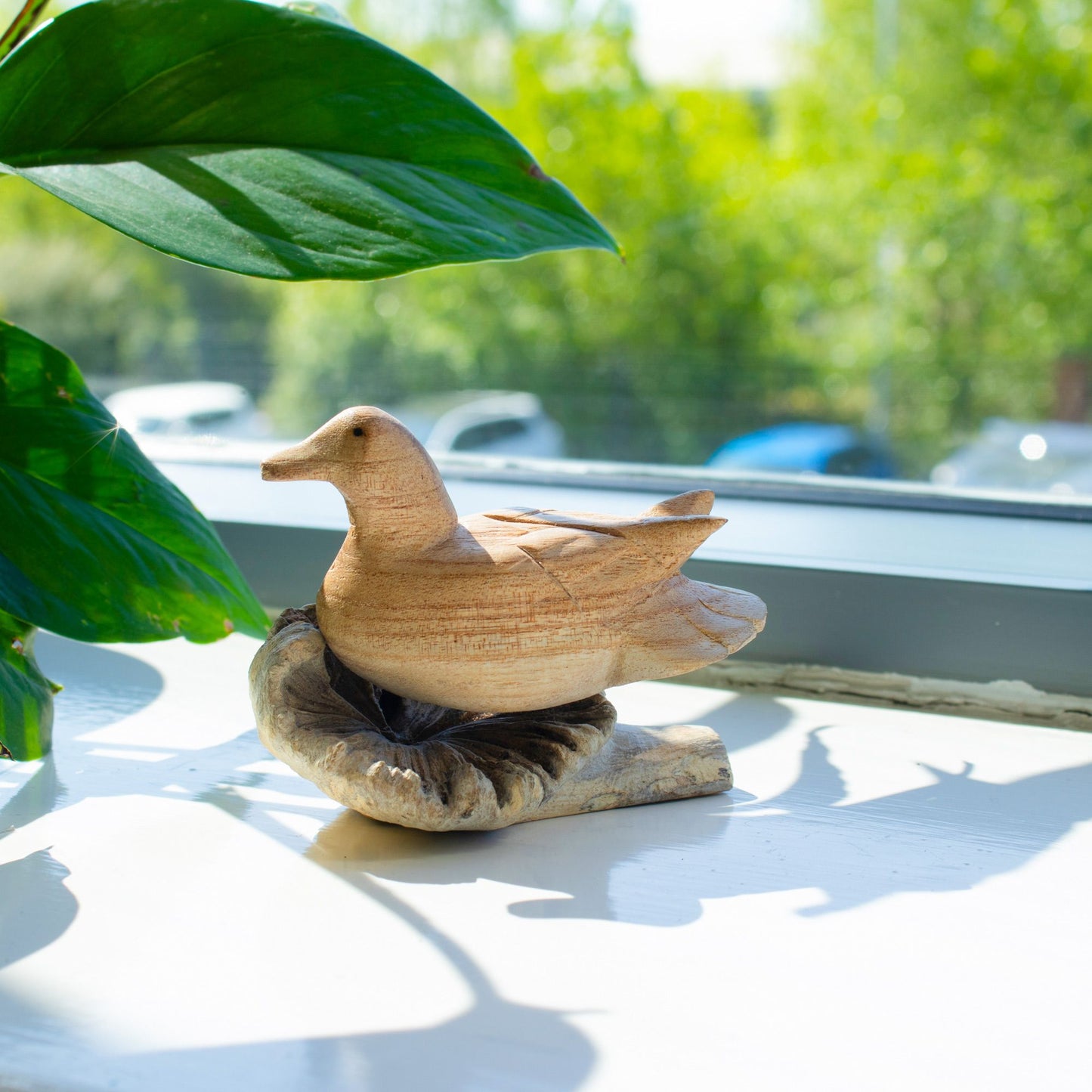 Handmade Parasite Wood Art Carving Wild Duck Resting with green leaves and blurred outdoor background
