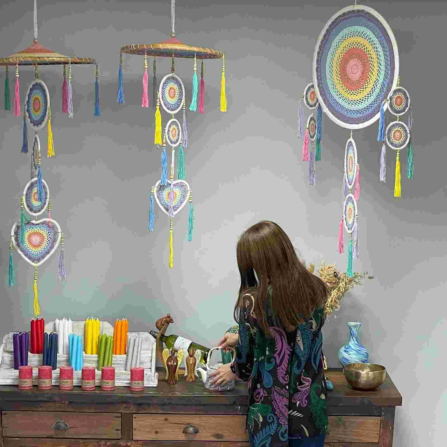 A woman in a colourful top standing in front of a wall with hanging dream catchers.