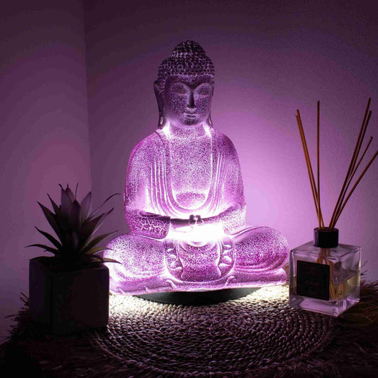 Meditation Buddha Lamp Lavender Crackle with the light turned on, accompanied by a small plant and diffuser on a textured surface.