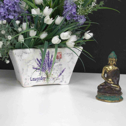 Decorative planter with lavender and tulips next to a Mini Brass Buddha Figurine, Sitting Meditating 