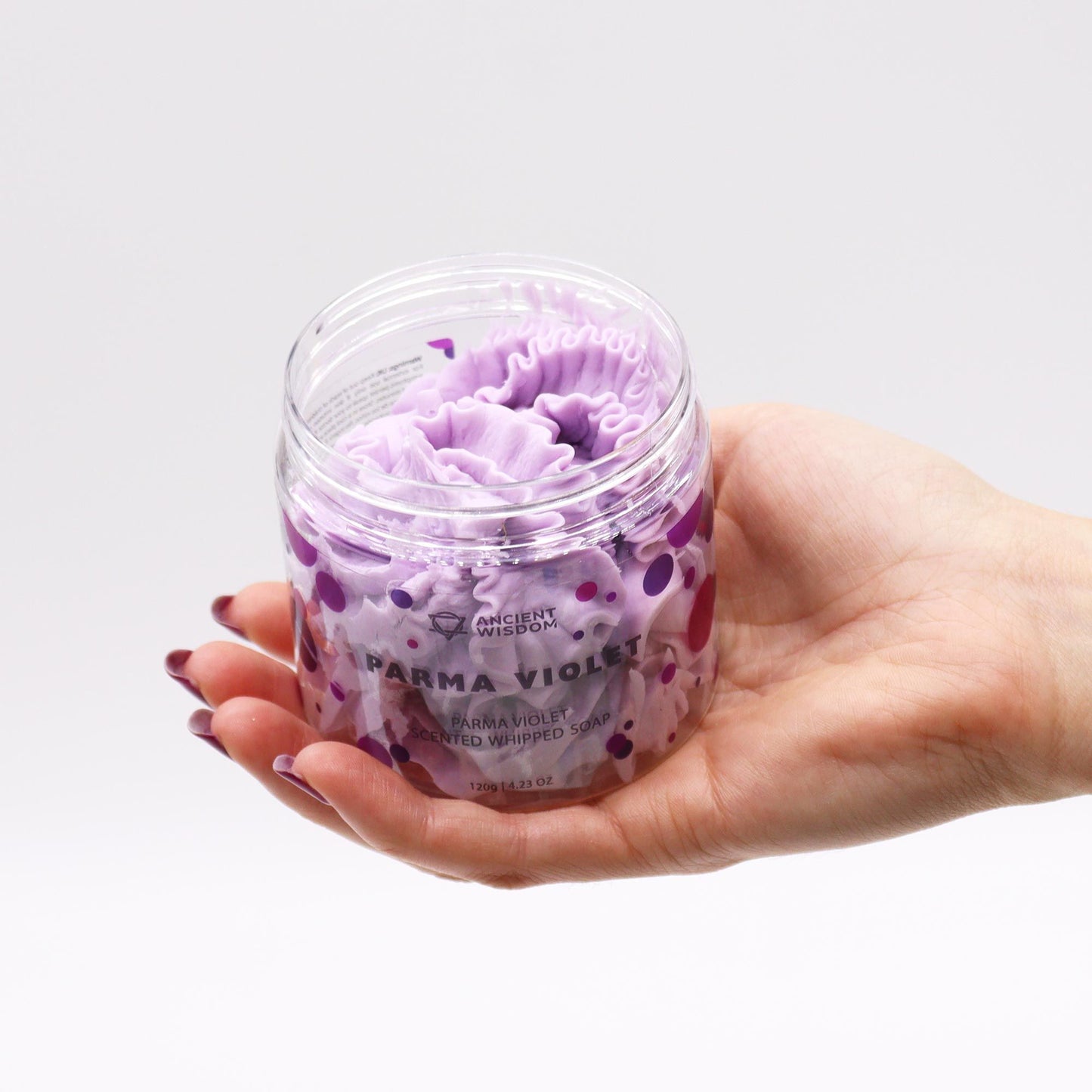 Hand holding a jar of purple whipped soap labeled 'Parma Violet' against a light gray background