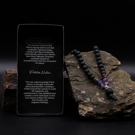 Essence of the Volcano Necklace on a rock next to an information card on a dark background