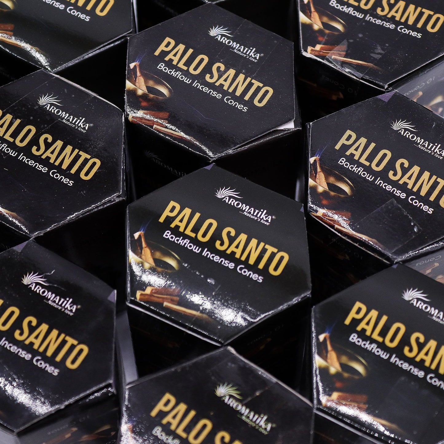 Piled boxes of Aromatika Palo Santo backflow incense cones on a dark background