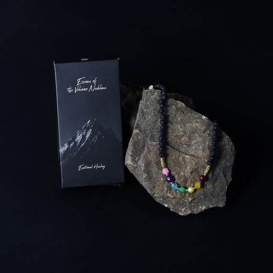 Necklace with colorful beads on a rock next to a box labeled 'Exodus of the Volcano Necklace' on a black background