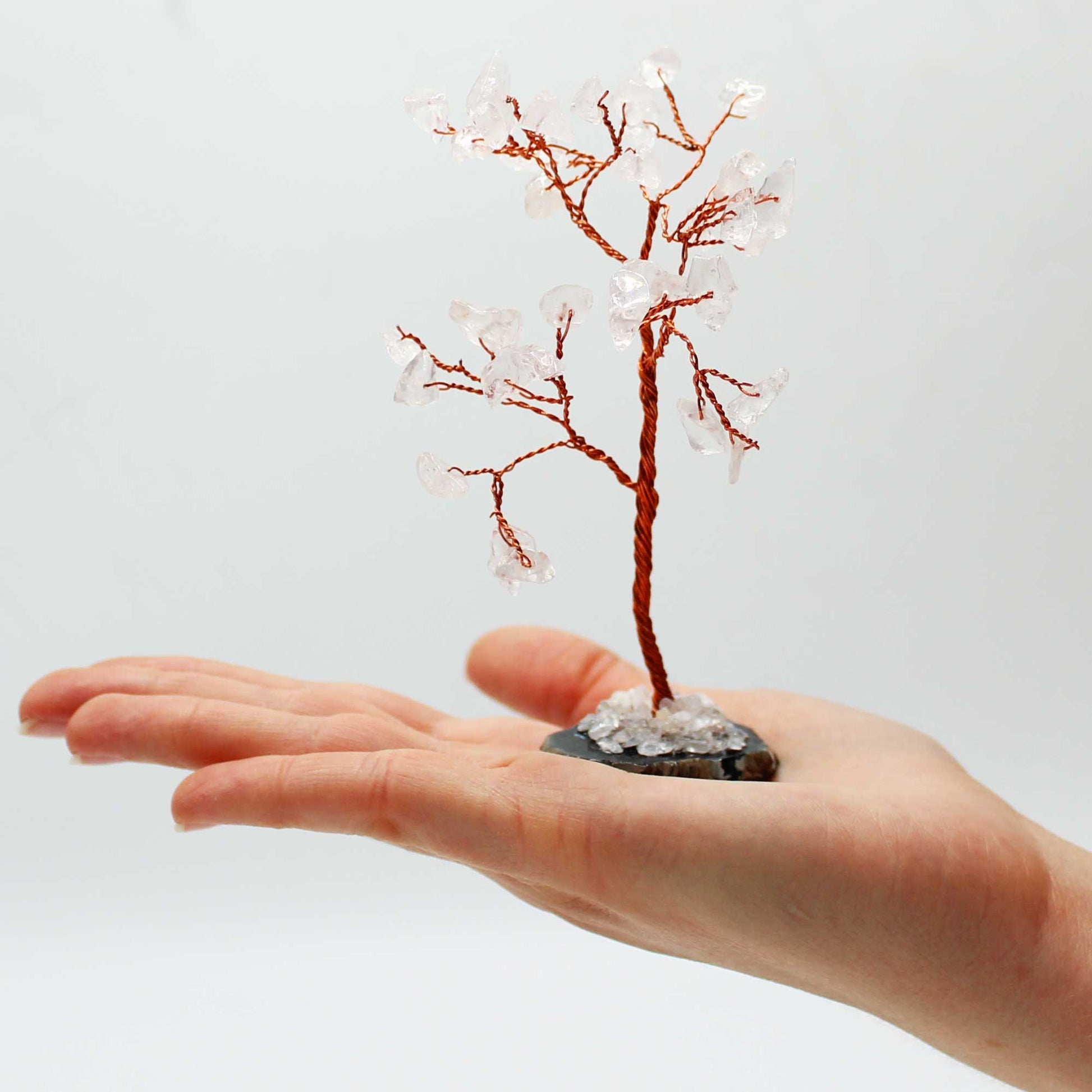 Hand holding a small decorative tree with copper branches and clear beads against a light background