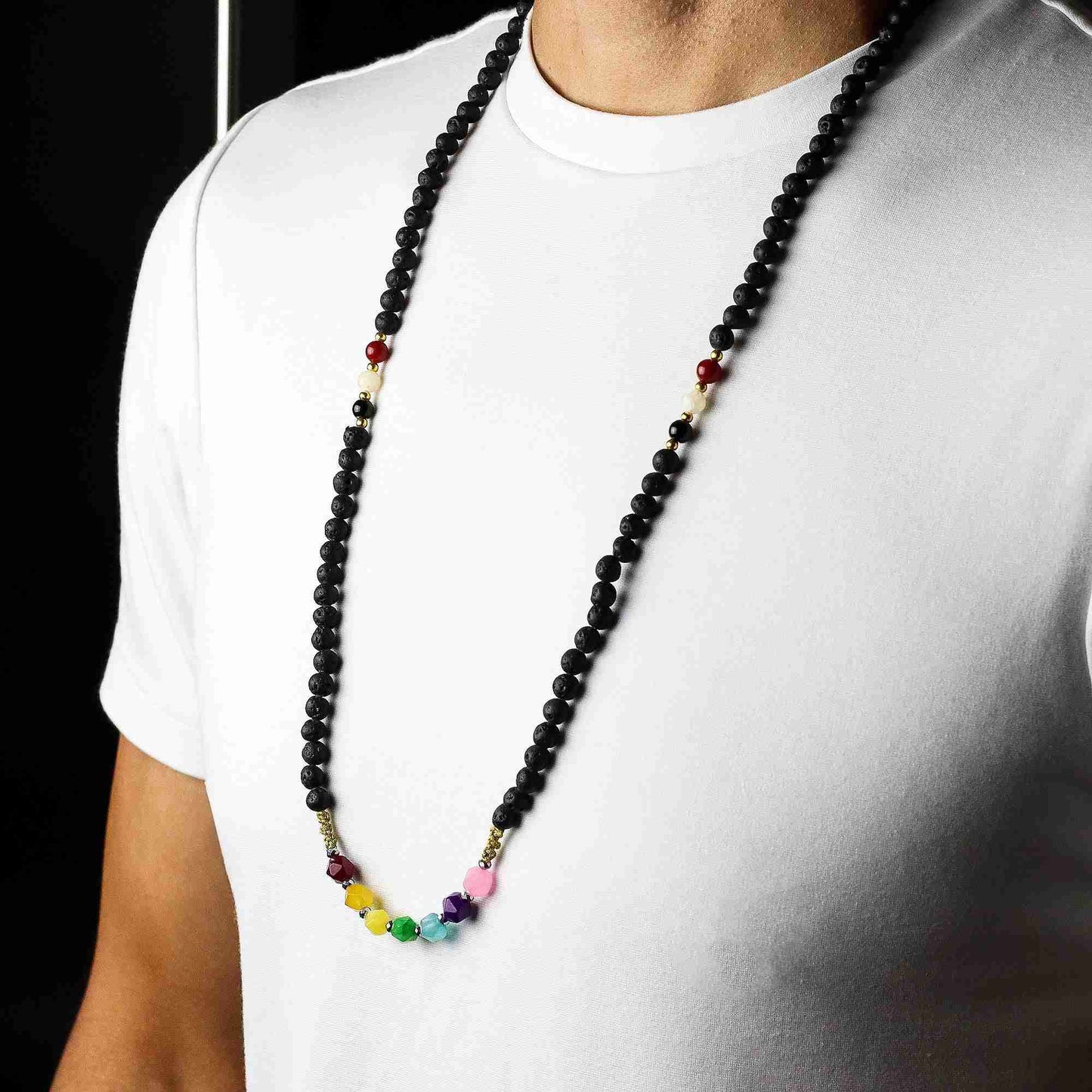 Person wearing a long beaded necklace with black, red, yellow, and multicolor beads on a white shirt.