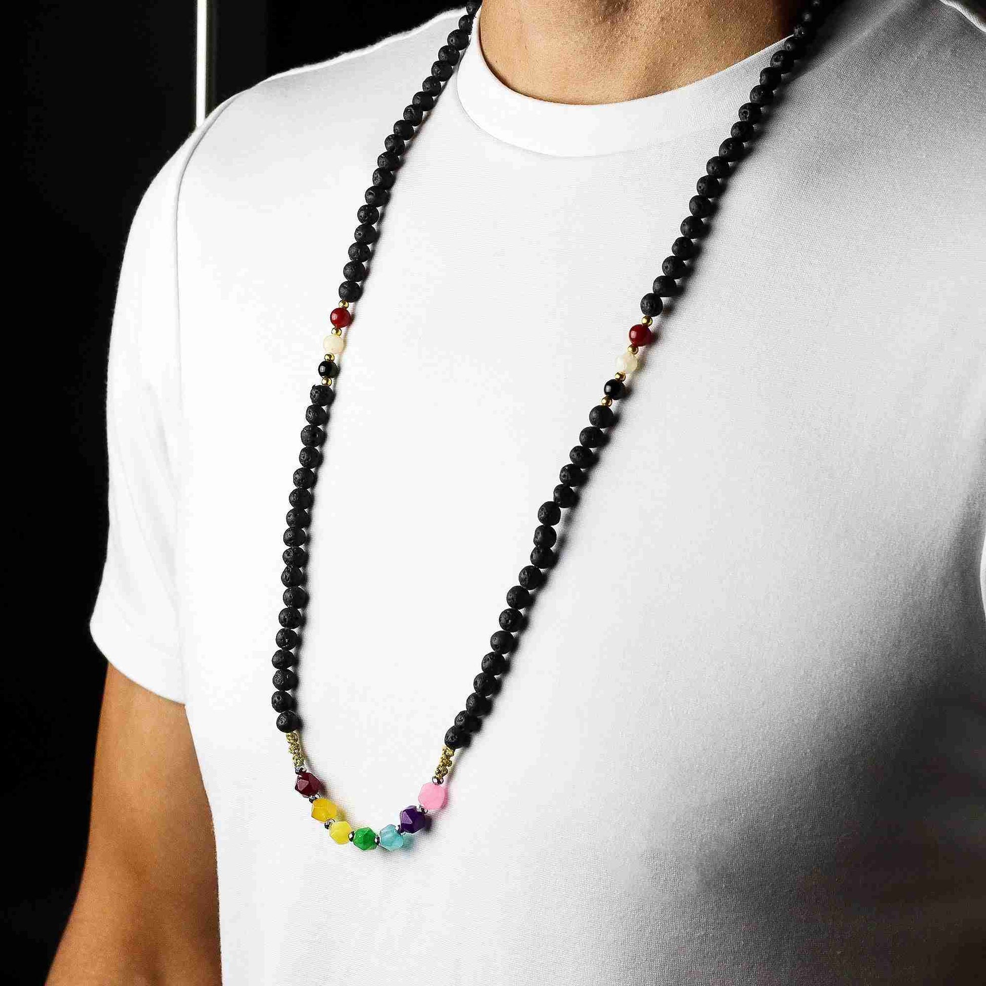 Person wearing a long beaded necklace with black, red, yellow, and multicolor beads on a white shirt.
