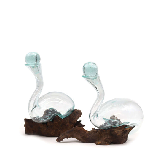 Two glass swans on a wooden base with a white background