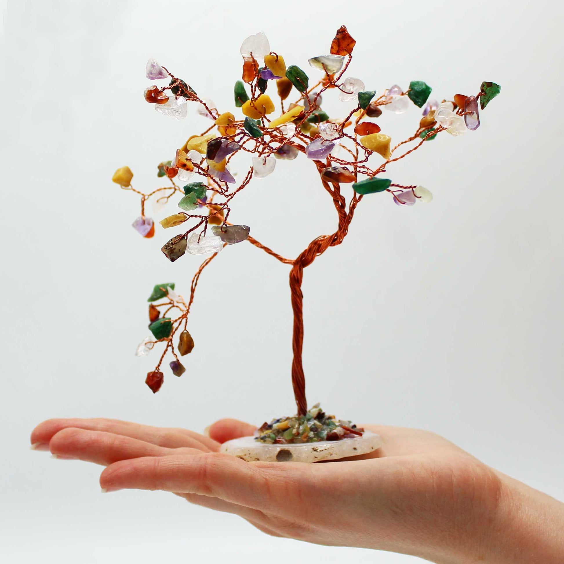 Hand holding a small tree made of multicolored stones against a white background