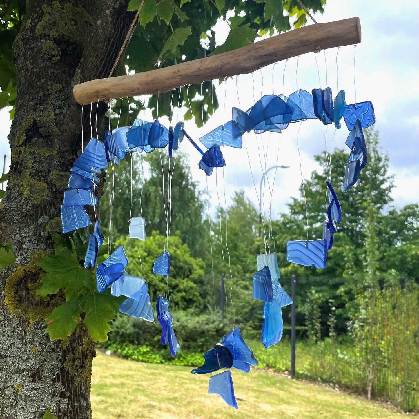 Recycled Glass Wind Chime - Blue hanging from a tree branch outdoors.