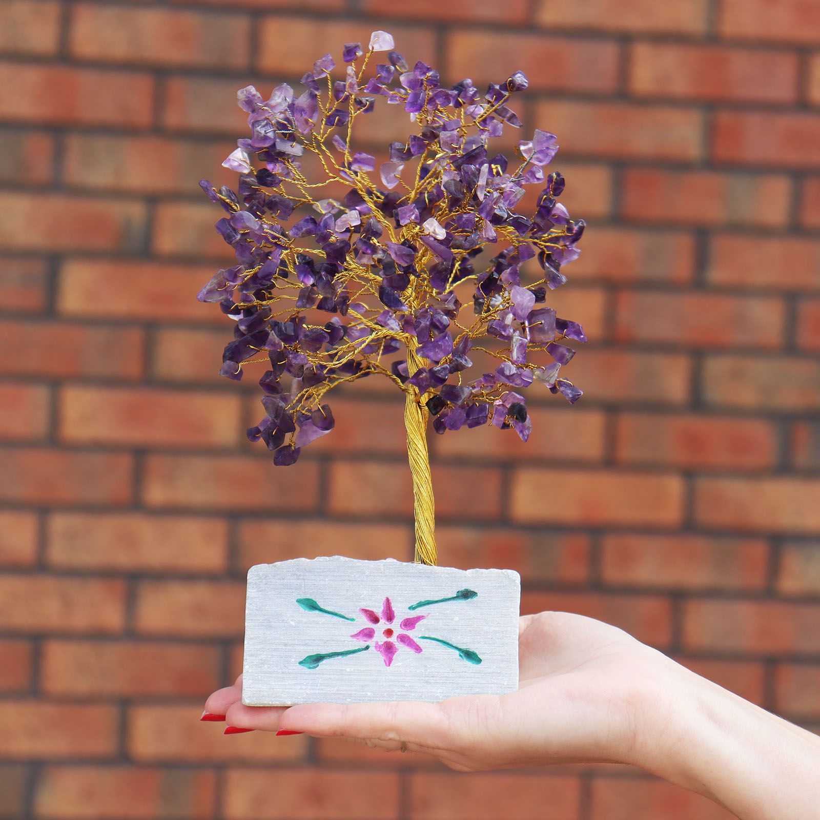 Hand holding an Indian Gemstone Tree - Amethyst (320 Stones) against a brick wall.