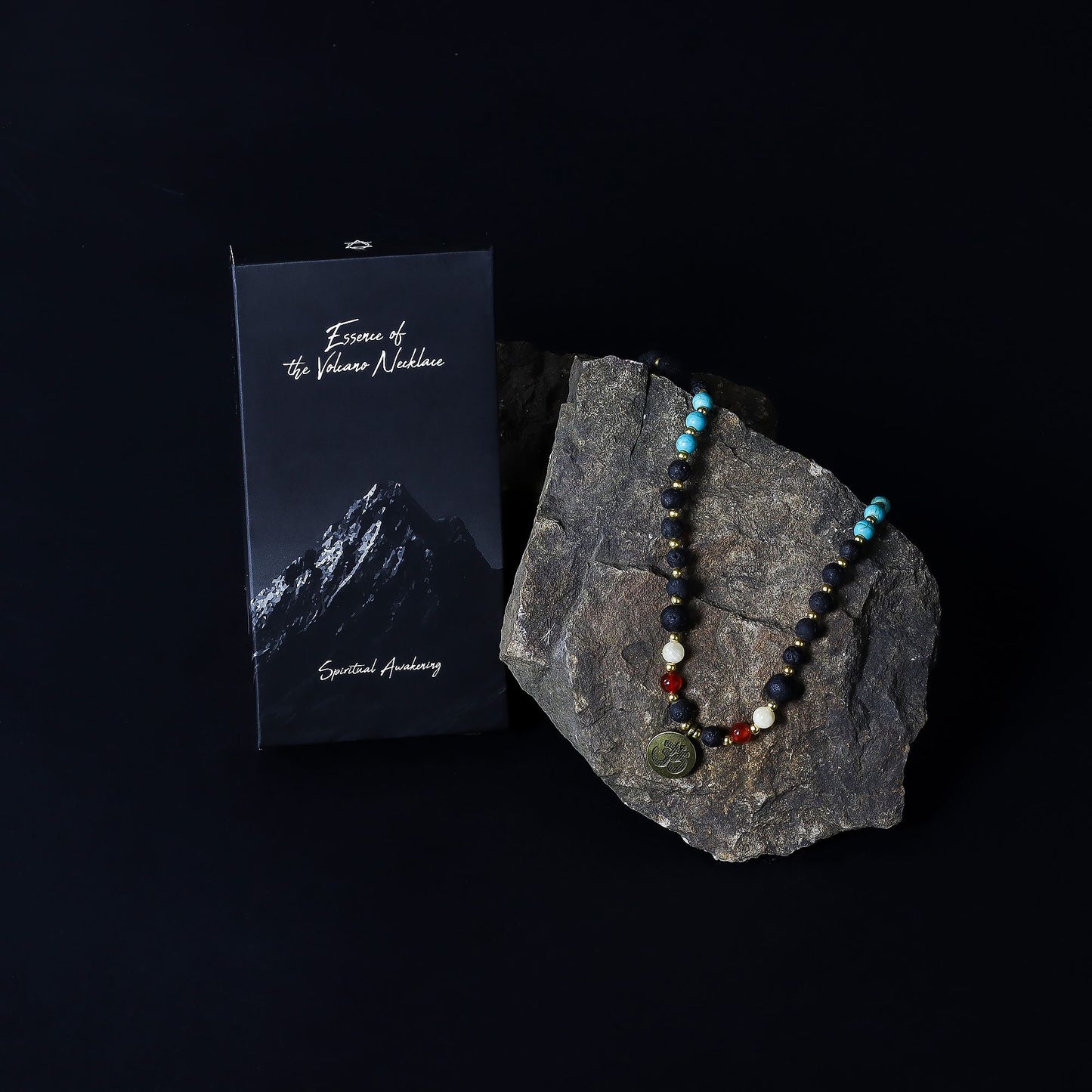 Essence of the Volcano Necklace - with beads on a rock next to a card with mountain imagery on a black background