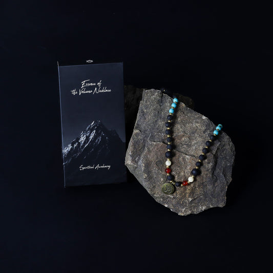 Essence of the Volcano Necklace - with beads on a rock next to a card with mountain imagery on a black background