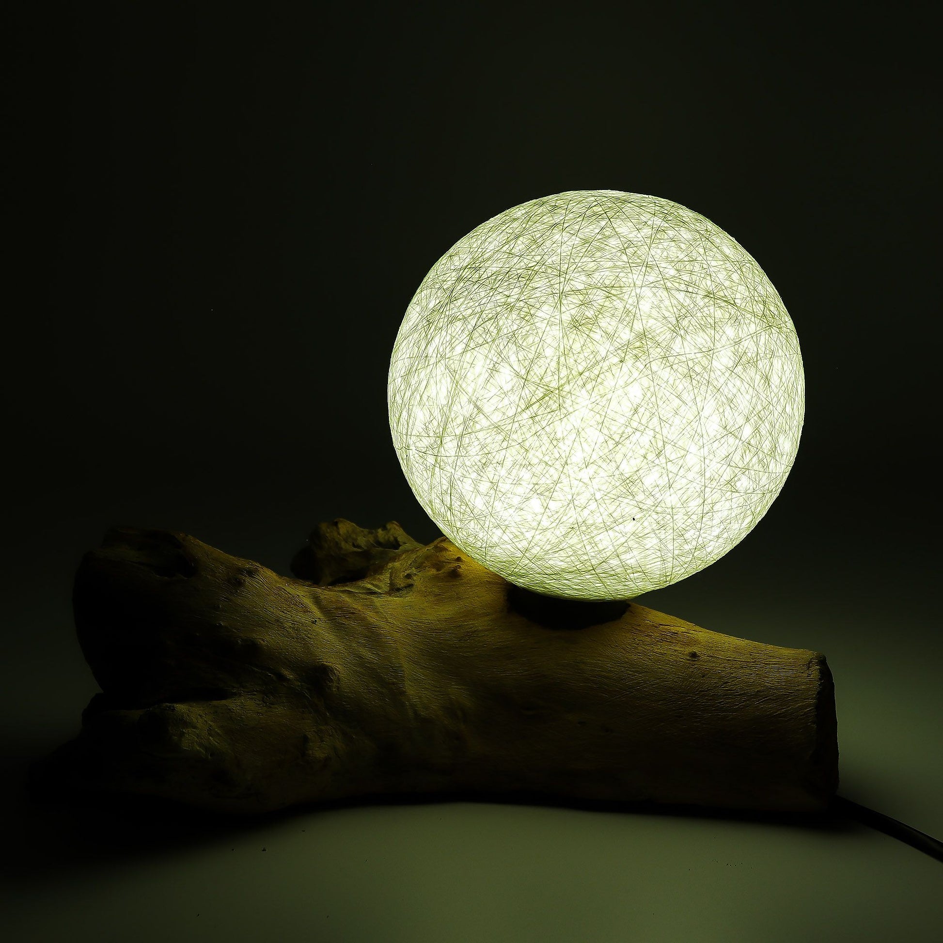 Spherical light bulb on a wooden log against a dark background