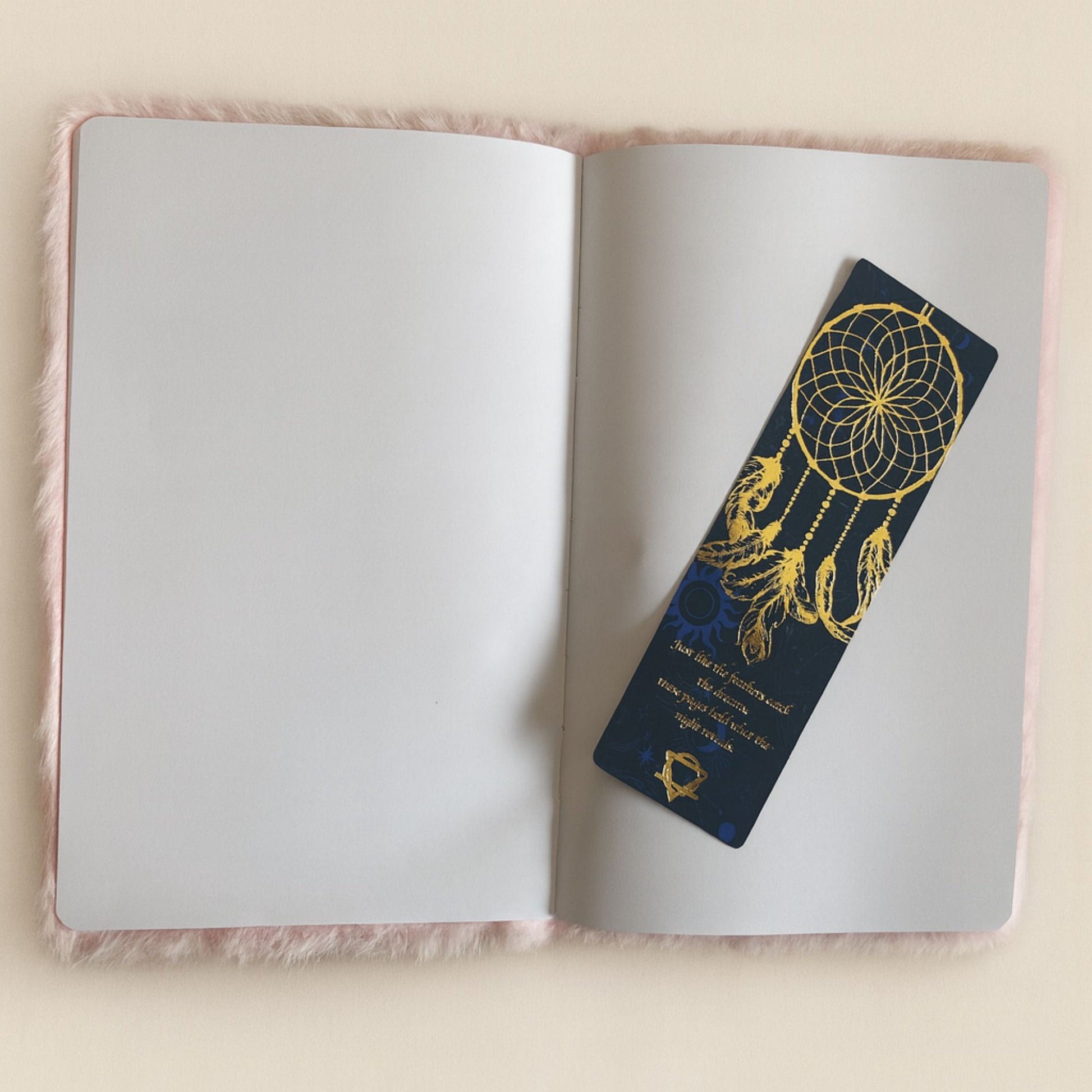 Open notebook with a decorative bookmark featuring a dreamcatcher design on a light pink surface.