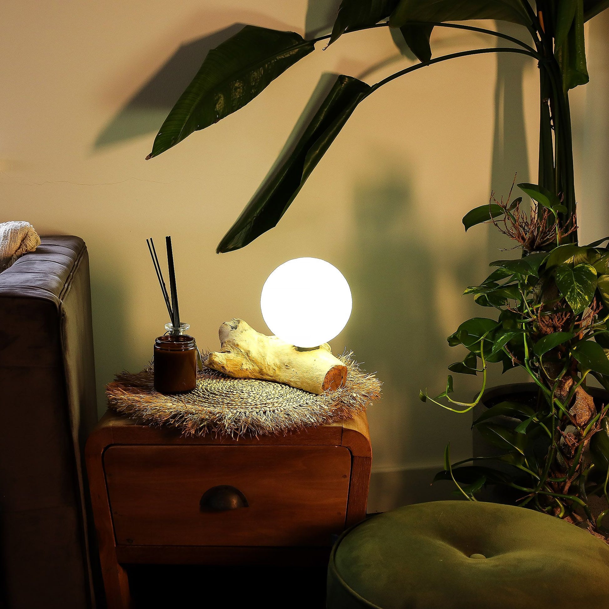 Glowing spherical lamp on a wooden side table with plants and a couch in the background